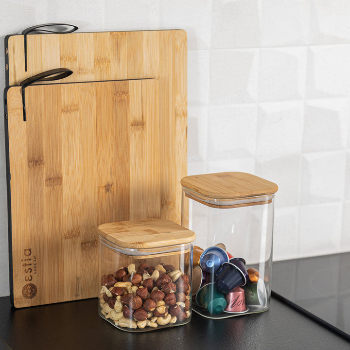 Γυάλινα δοχεία αποθήκευσης με καπάκι bamboo δίπλα σε ξύλινες επιφάνειες κοπής και διακοσμητικά κουζίνας.