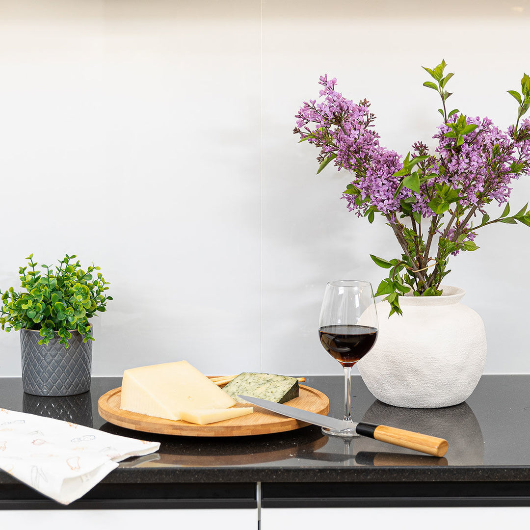 Βάση τυριών Bamboo Essentials Estia τοποθετημένη σε πάγκο κουζίνας με κρασί, μαχαίρι και διακόσμηση με λουλούδια.