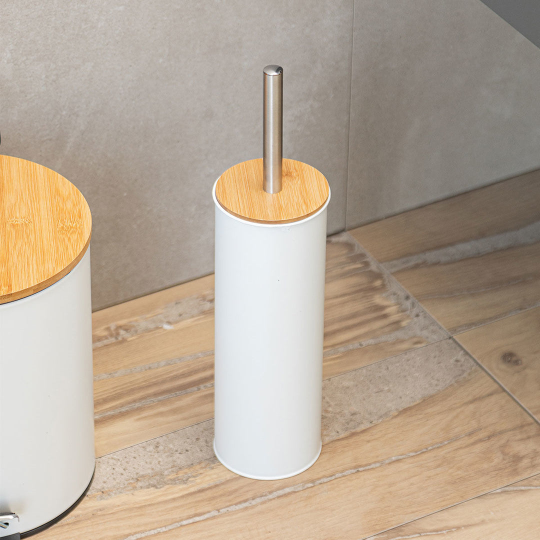 Λευκό πιγκάλ με καπάκι bamboo και μεταλλικό χερούλι, τοποθετημένο σε ξύλινο δάπεδο μπάνιου δίπλα σε λευκή μπανιέρα.