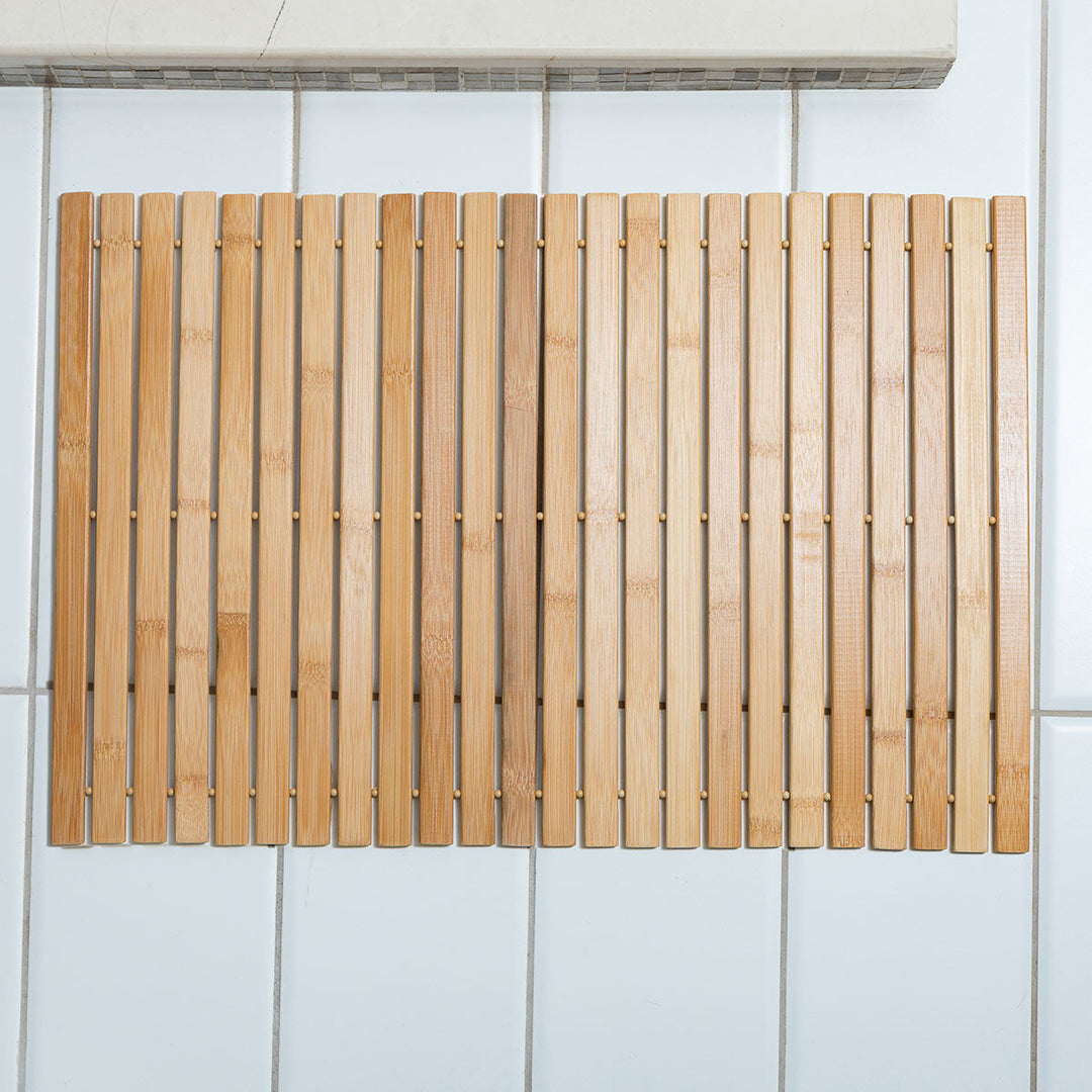 Ξύλινο bamboo χαλάκι μπάνιου τοποθετημένο σε λευκό πλακάκι, με κάθετες λωρίδες και φυσική απόχρωση ξύλου.