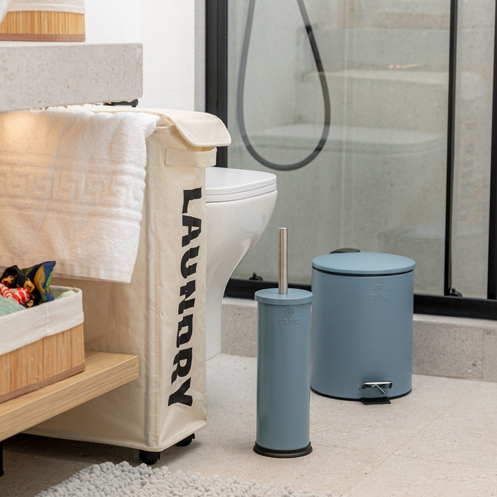 Μπάνιο με μπεζ καλαθάκι απλύτων LAUNDRY δίπλα σε λευκή λεκάνη, γκρι ντουζιέρα και γαλάζιο πιγκάλ με μεταλλική λαβή.