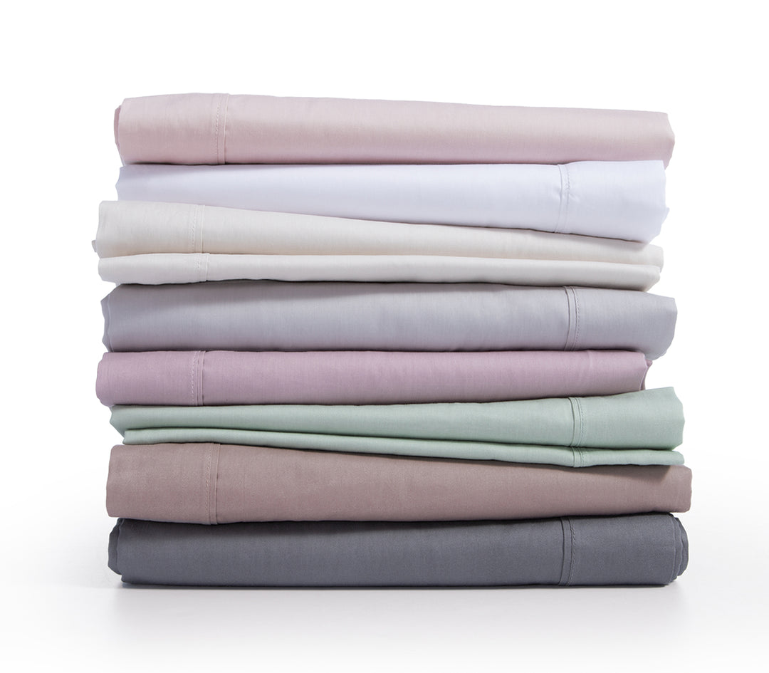 Στοίβα από βαμβακερά σεντόνια σε διάφορα παστέλ και ουδέτερα χρώματα, όπως ροζ, λευκό, εκρού, γκρι, λιλά, μέντα, καφέ και ανθρακί.