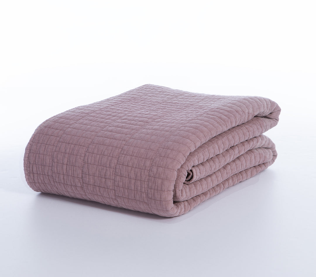 Διπλωμένο κουβερλί σε dusty pink απόχρωση με καπιτονέ ραφές σε λευκό φόντο.