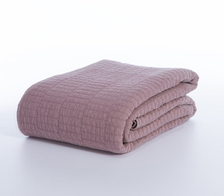 Διπλωμένο κουβερλί σε dusty pink απόχρωση με καπιτονέ ραφές σε λευκό φόντο.