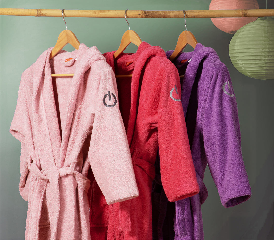 Παιδικά μπουρνούζια με κουκούλα και ζώνη, σε ροζ, κόκκινο και μοβ χρώμα, κρεμασμένα σε ξύλινες κρεμάστρες