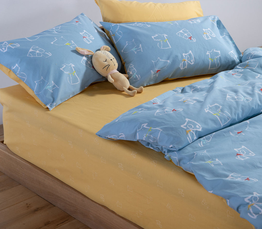 Λεπτομέρεια παιδικών σεντονιών Dog Life της Nef-Nef Homeware με σκίτσα σκύλων σε μπλε φόντο και κίτρινο κατωσέντονο.