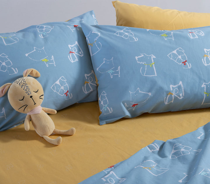 Κοντινή λήψη μαξιλαροθηκών Dog Life της Nef-Nef Homeware με σχέδια σκύλων και παιδικό λούτρινο παιχνίδι στο κρεβάτι.