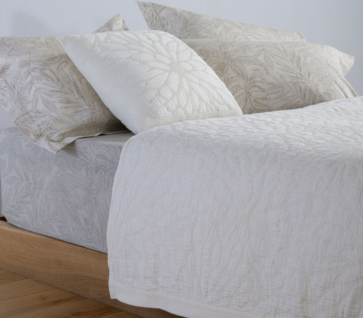 Διακοσμητική μαξιλαροθήκη Nef-Nef Homeware σε μπεζ-λευκή απόχρωση πάνω σε κρεβάτι, με ανάγλυφο φυτικό σχέδιο.