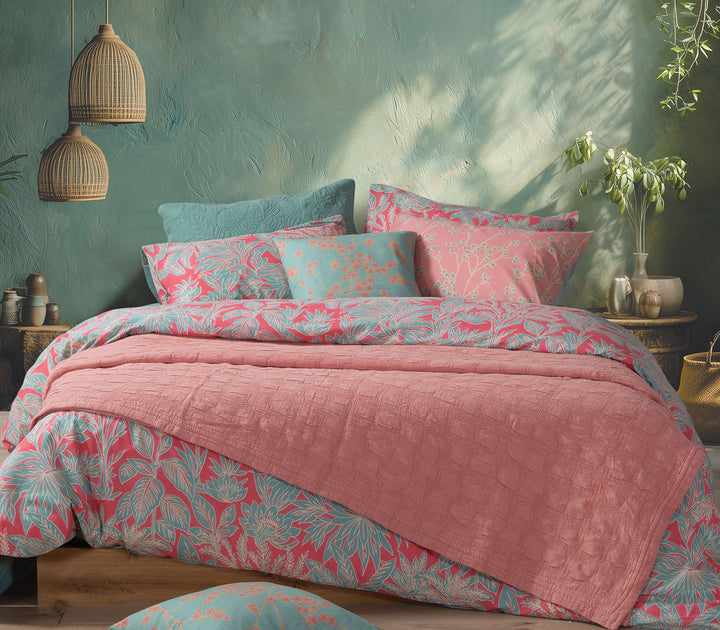 Κοραλί βαμβακερή κουβέρτα Nef-Nef Homeware στρωμένη πάνω σε κρεβάτι με πολύχρωμα διακοσμητικά μαξιλάρια σε φυσικό υπνοδωμάτιο.