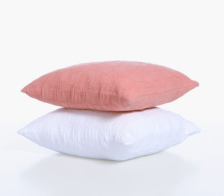 Διακοσμητικές μαξιλαροθήκες Nef-Nef Homeware σε κοραλί και λευκό χρώμα με ανάγλυφη υφή τοποθετημένες η μία πάνω στην άλλη σε λευκό φόντο.