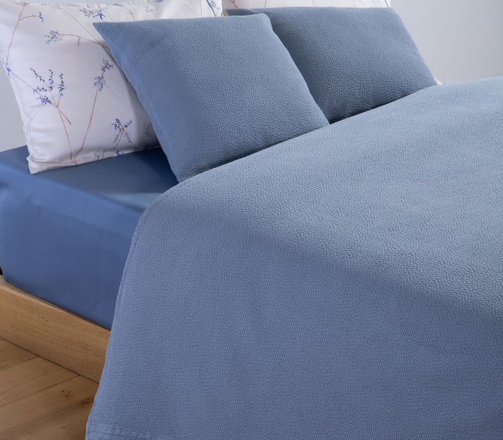 Υπέρδιπλη βαμβακερή κουβέρτα Nef-Nef Homeware σε μπλε χρώμα στρωμένη σε κρεβάτι με διακοσμητικά μαξιλάρια και σεντόνια με διακριτικό μοτίβο.