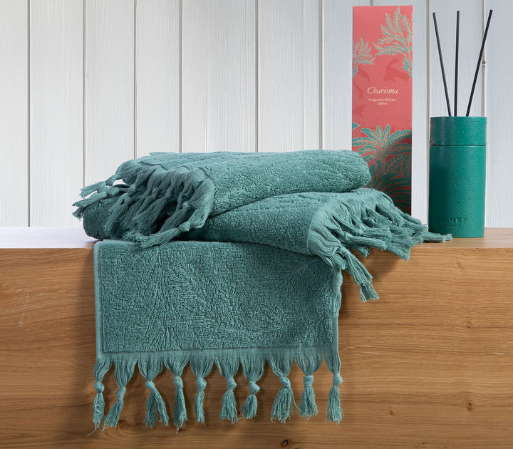 Πράσινες βαμβακερές πετσέτες Nef-Nef Homeware με κρόσσια τοποθετημένες σε ξύλινο πάγκο δίπλα σε αρωματικό χώρου.