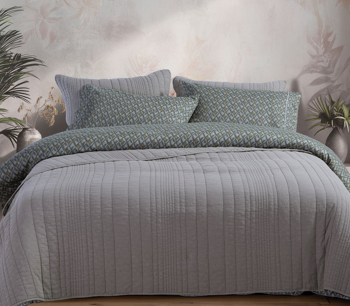 Γκρι καπιτονέ κουβερλί Nef-Nef Homeware στρωμένο σε κρεβάτι με διακοσμητικά μαξιλάρια και φυσικά διακοσμητικά φυτά.