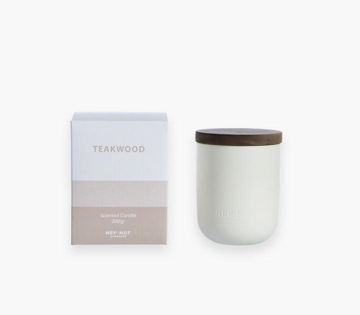 Αρωματικό χώρου με στικς Teakwood της Nef-Nef Homeware δίπλα σε αρωματικό κερί πάνω σε τραπεζάκι μπροστά από καναπέ.