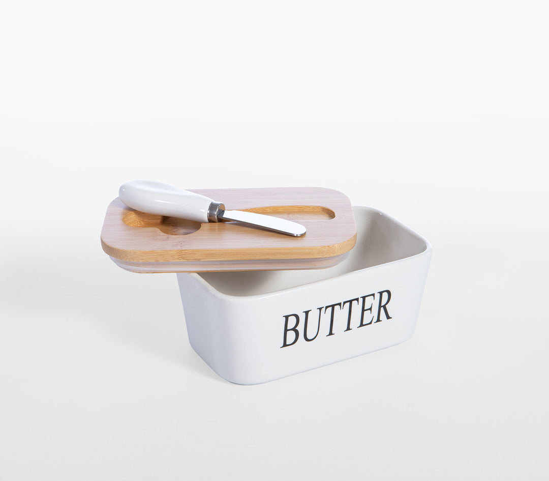 Κεραμικό δοχείο βουτύρου με επιγραφή butter και ξύλινο καπάκι σε τραπέζι με υφάσματα και σκεύη.