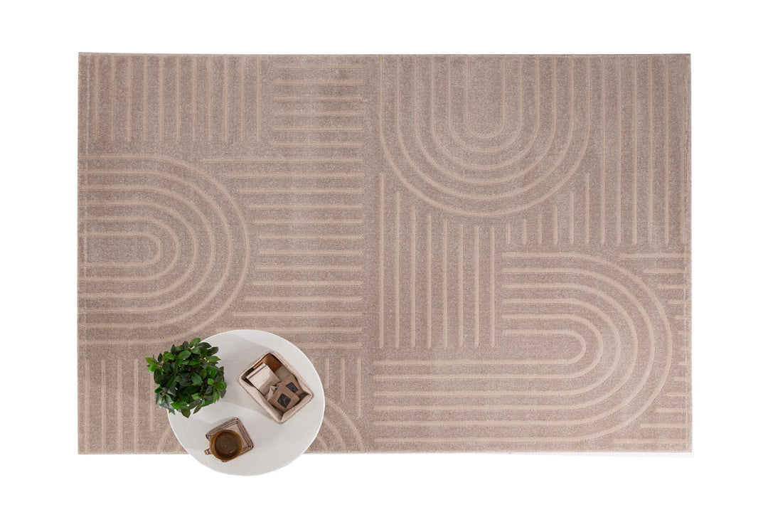 Μπεζ χαλί Organic Royal Carpet με γεωμετρικές γραμμές και καμπύλες, πλαισιωμένο από λευκό στρογγυλό τραπέζι με φυτό και κουτί οργάνωσης.