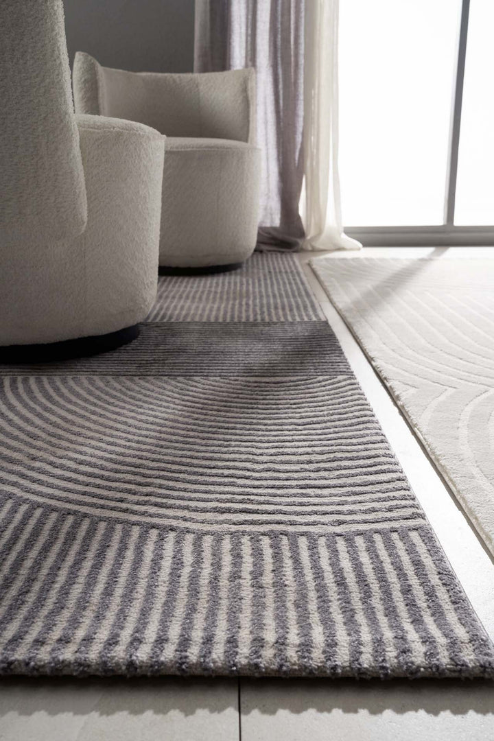 Μοντέρνο χαλί Organic της εταιρείας Royal Carpet σε γκρι και εκρού αποχρώσεις με γεωμετρικό σχέδιο γραμμών, τοποθετημένο σε minimal σαλόνι με λευκές πολυθρόνες.