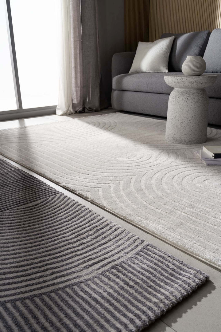 Χαλί Organic Royal Carpet σε λευκή και γκρι απόχρωση με ανάγλυφο γεωμετρικό μοτίβο, σε σαλόνι με γκρι καναπέ και γυάλινη μπαλκονόπορτα.