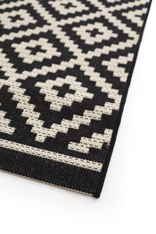 Λεπτομέρεια υφής μαύρου και εκρού χαλιού με γεωμετρικό μοτίβο από ρόμβους και πλαισίωση στις άκρες.