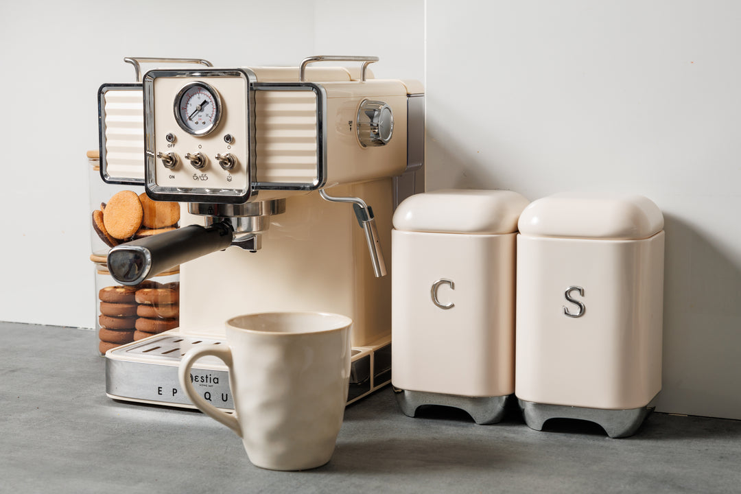 Vintage μηχανή espresso σε εκρού απόχρωση πάνω σε πάγκο κουζίνας, με ποτήρι μπισκότων και δοχεία καφέ, ζάχαρης.