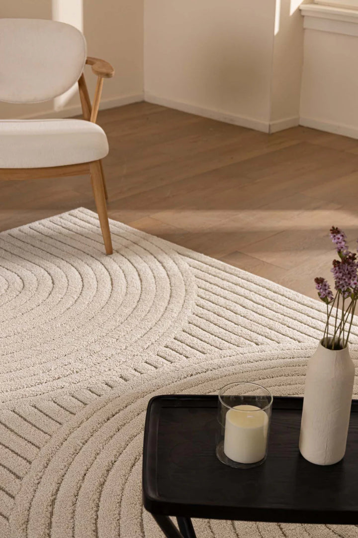 Χαλί Chiara σε ουδέτερη εκρού απόχρωση, στρωμένο σε σαλόνι με minimal διακόσμηση, ξύλινο πάτωμα και λουλούδια σε βάζο.